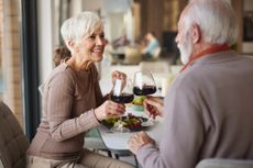 Happy senior woman toasting with her husband while having a meal at dining table. the scene could be at a fancy restaurant or an upscale senior living community.