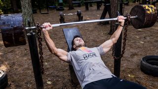 Fit young man doing a bench press on a DIY weight bench outdoors