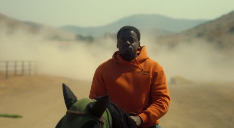 Dark-skinned Black Man wearing an overage hoodie sits on brown horse