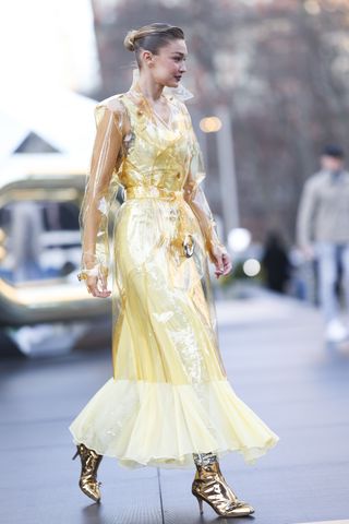 A photo of Gigi Hadid modeling a yellow Rabanne ensemble accessorized with metallic gold boots.