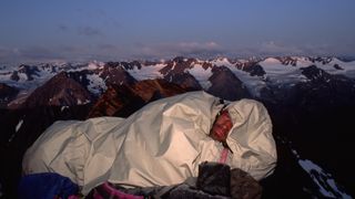A man sleeping in a bivy sack with snowy mountains in the background
