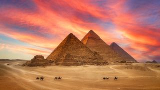 A camel caravan crosses in front of the great pyramids at Giza with a stunning sunrise in the background.