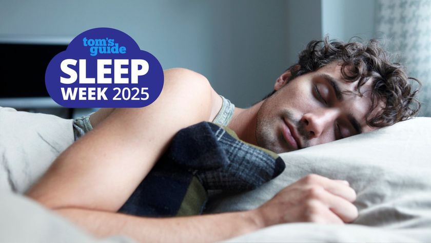 The image shows a curly haired man sleeping on his side while clutching a stuffed animal 