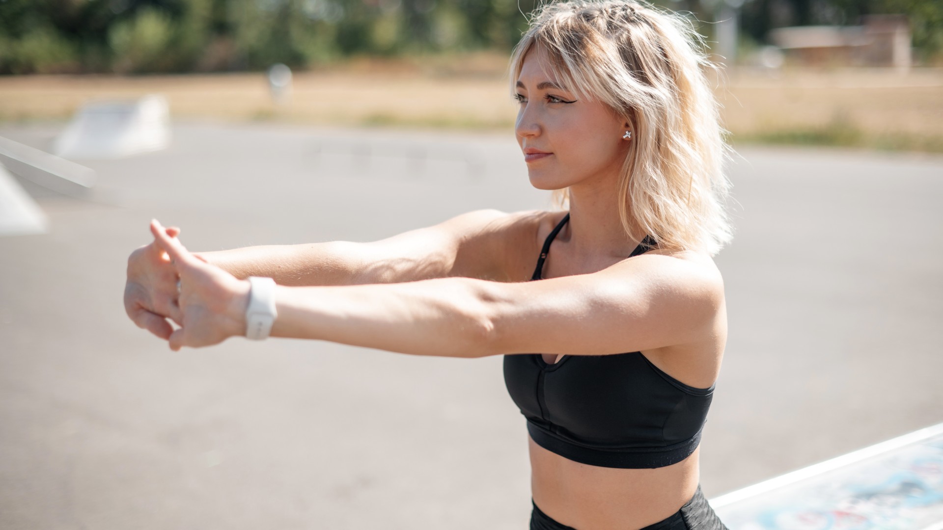 Young woman outdoors with hands interlaced stretching her shoulders with arms extended in front of her