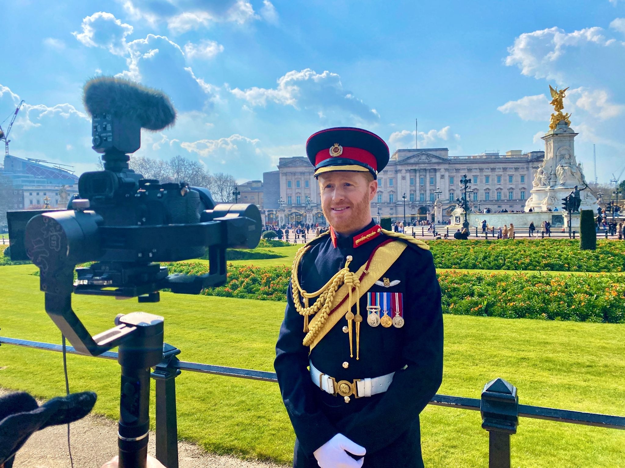 Prince Harry impersonator Rhys Whittock standing in front of Buckingham Palace and a video camera