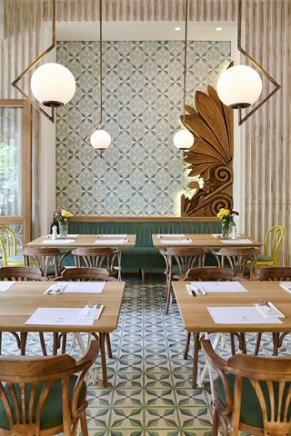 Restaurant interior with green and blue patterned tiled on the wall and floor and wooden tables and chairs