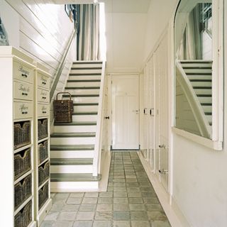 White-wall hallway with white cabinets and woven baskets with a white mirror and a white staircase