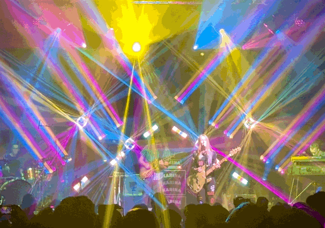 a rock band on stage in a crowded night club full of multicolored lights