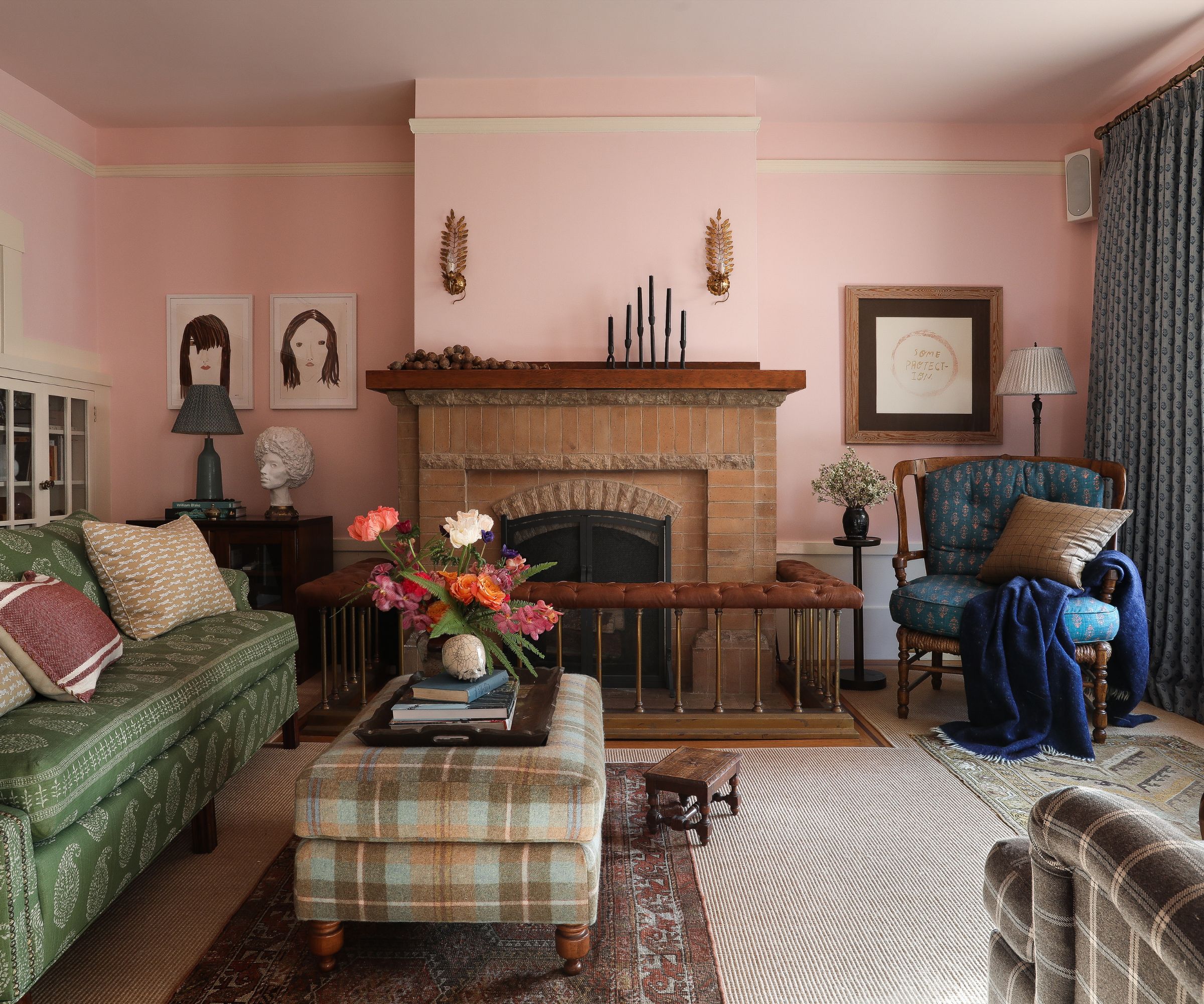traditional cozy living room with pink walls, green sofa, brick fireplace, and plaid ottoman