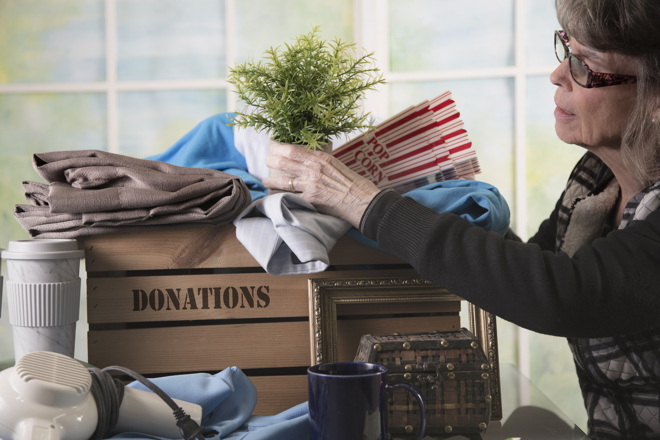 An older woman puts an artificial plant in a box marked Donations.