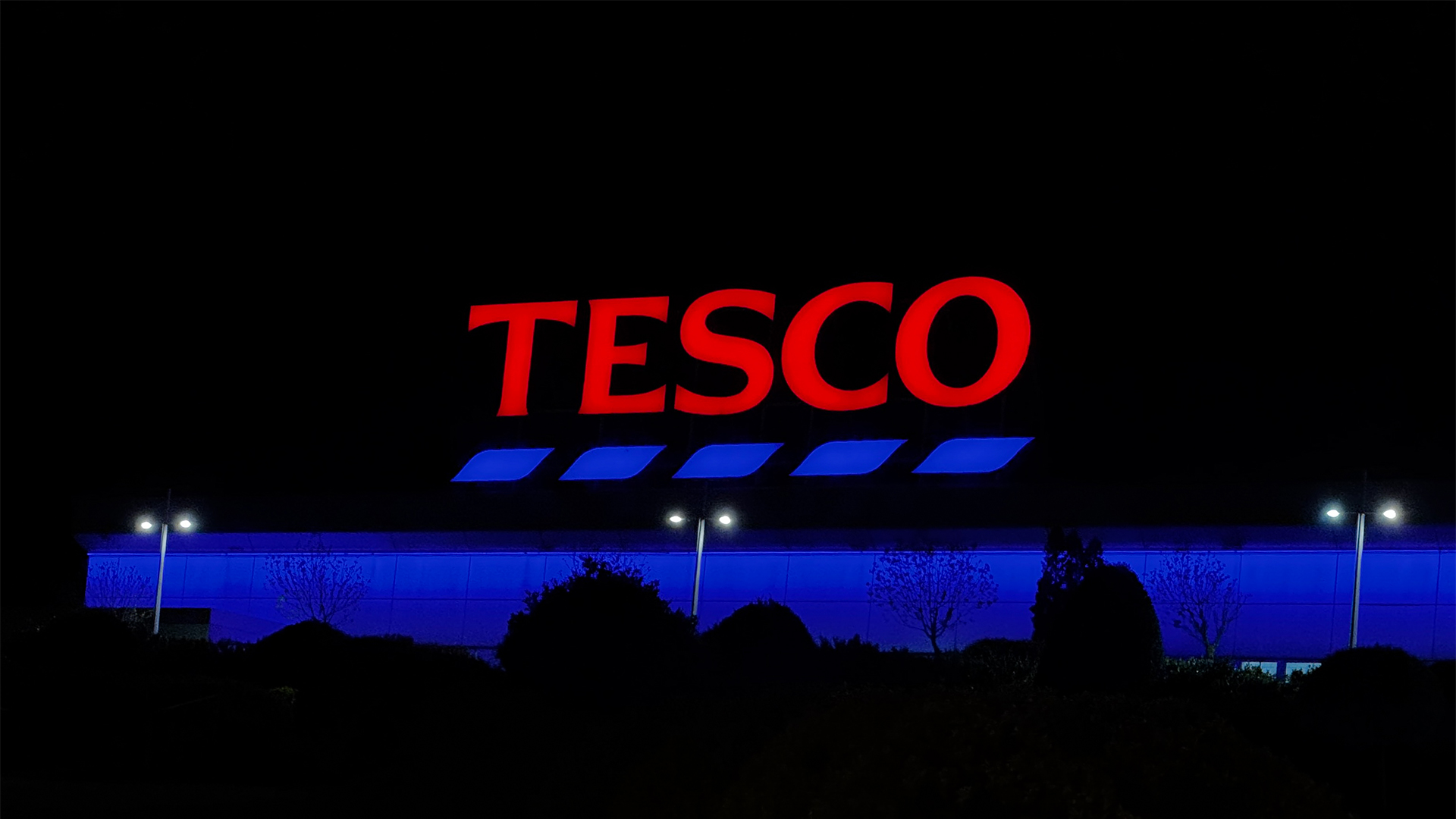 Tesco supermarket logo and branding pictured on a sign illuminated at night at a shopping mall in Budapest, Hungary.