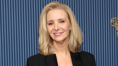 Image of Lisa Kudrow smiling with blonde side-part bob and wearing a black tailored jacket, with blue striped background