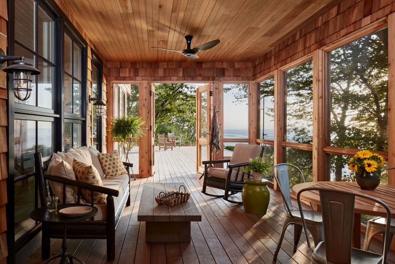 sunroom with lake view and vintage furniture pine wood walls and floor doors open to deck and sunflowers in vase 