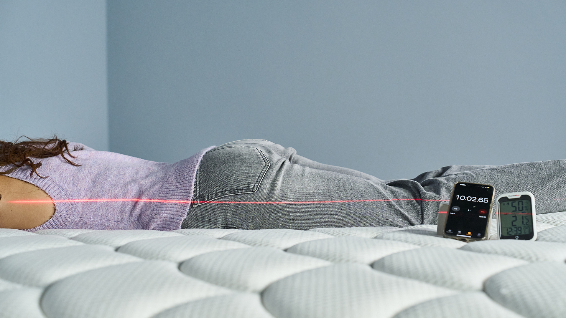 A Tom's Guide Tester lies on her front on the DreamCloud Classic mattress. A red line from a laser is seen along the side of her body to measure how straight her spine is.