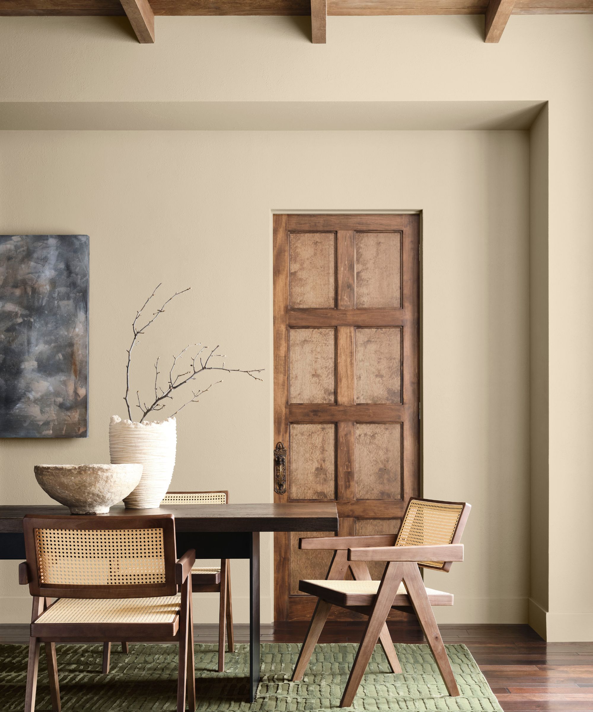 Dining room painted in Sherwin-Williams&#039; Universal Khaki with a large wooden table and rattan dining chairs
