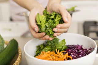 Hands putting fresh lettuce into a bowl with different vegetables