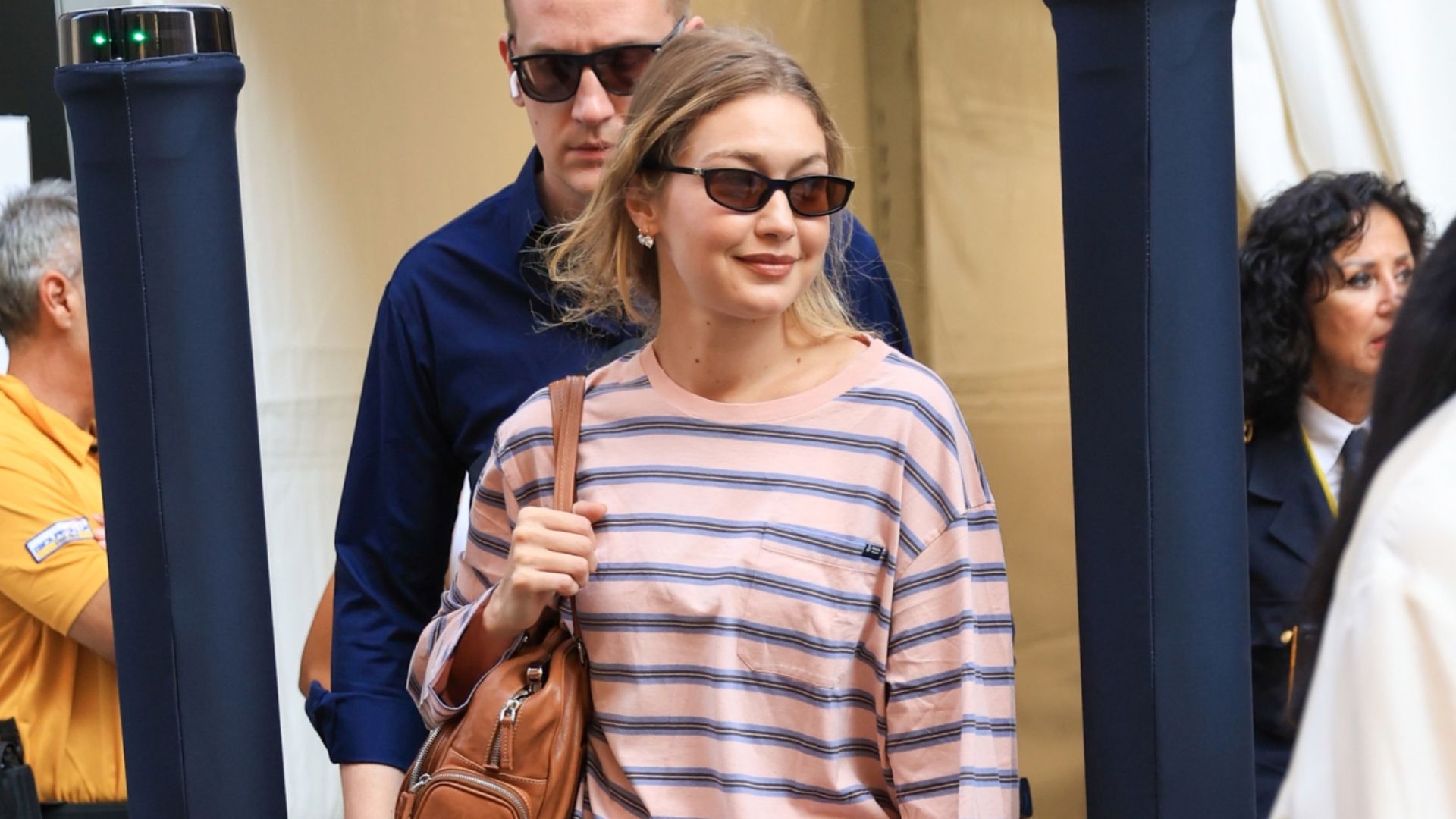 Gigi Hadid walks down the street in Milan wearing brown straight leg jeans with loafers and a striped t-shirt.