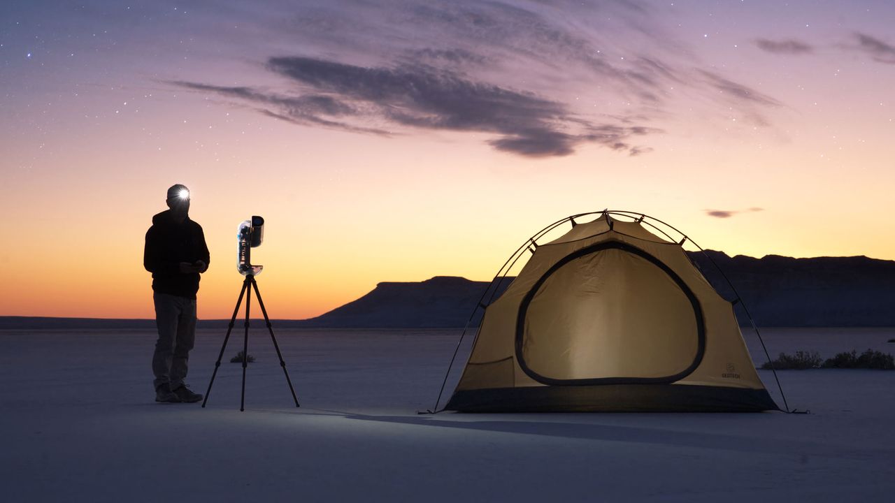 A man standing next to the Vaonis Vespera II - X edition and a tent with a sunset in the background.