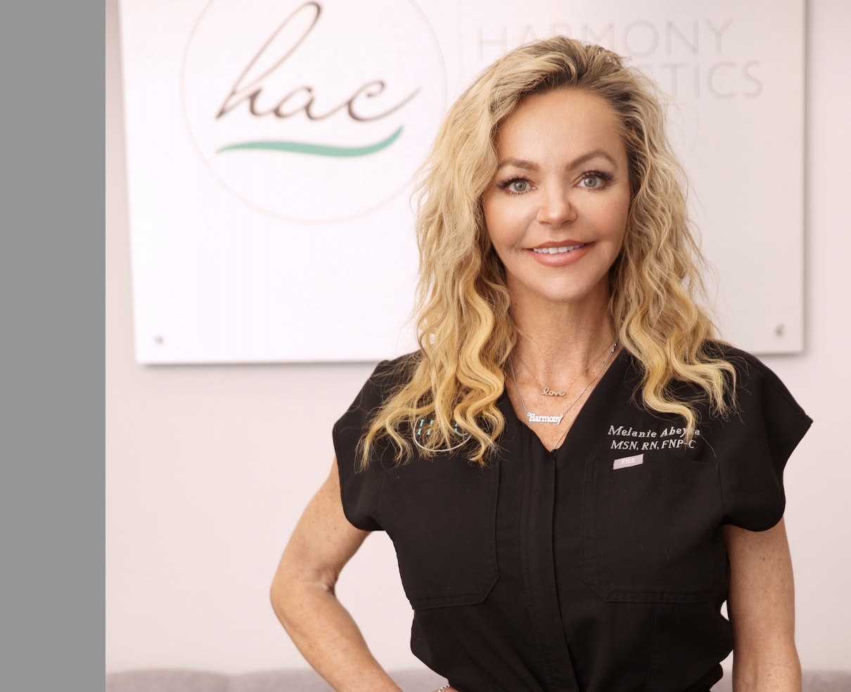 a white woman in black scrubs with blonde curly hair smiling at the camera