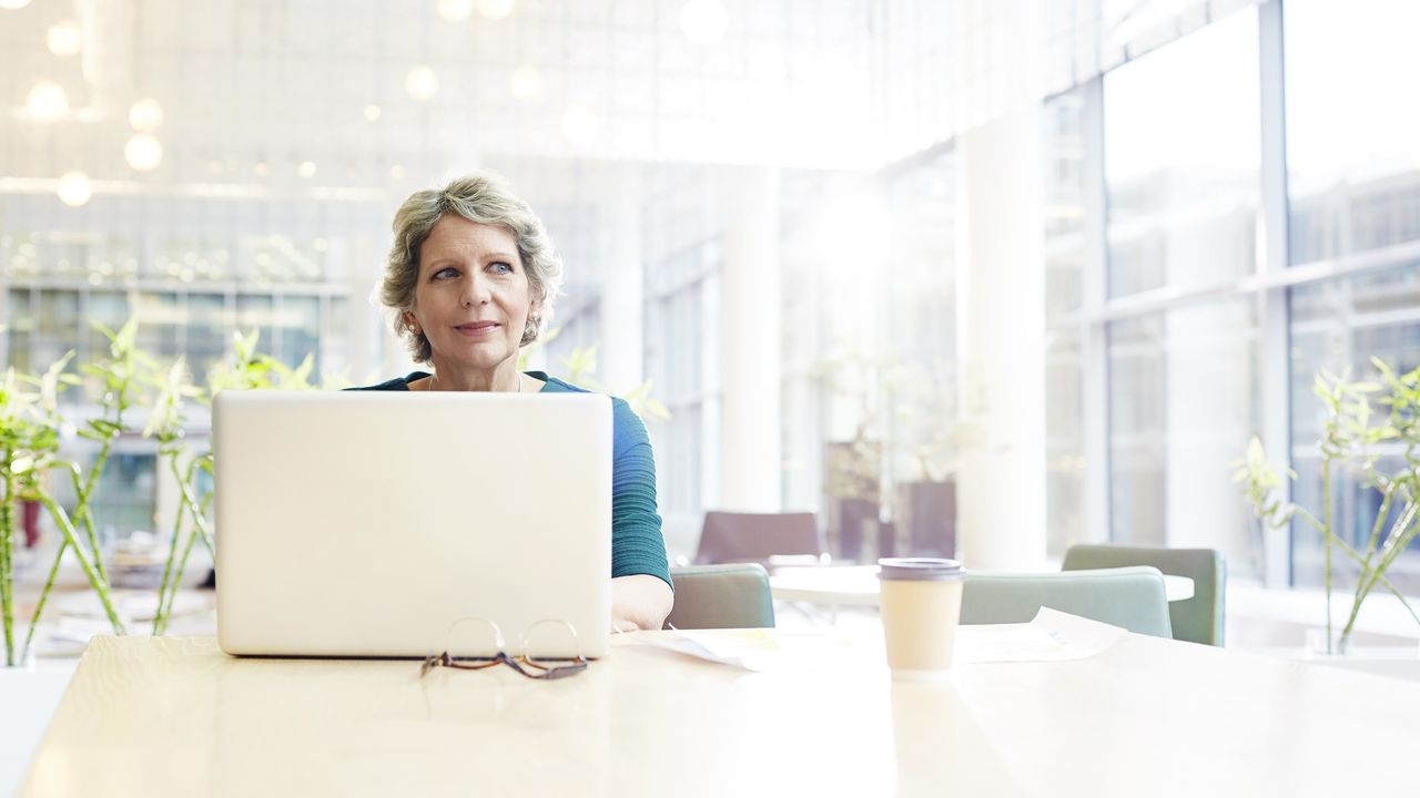 A woman looks thoughtful while working on her laptop at a table.