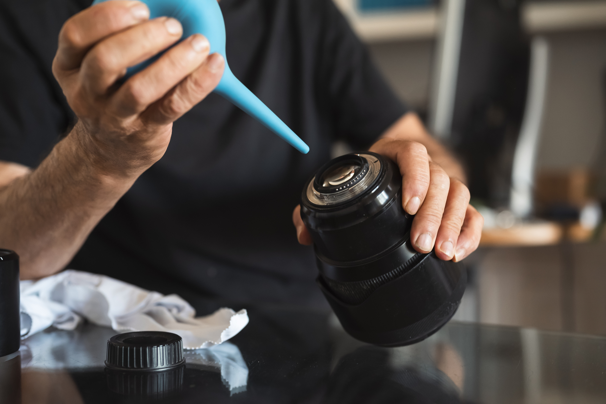 A man using a blue air puffer to clean the back of a lens