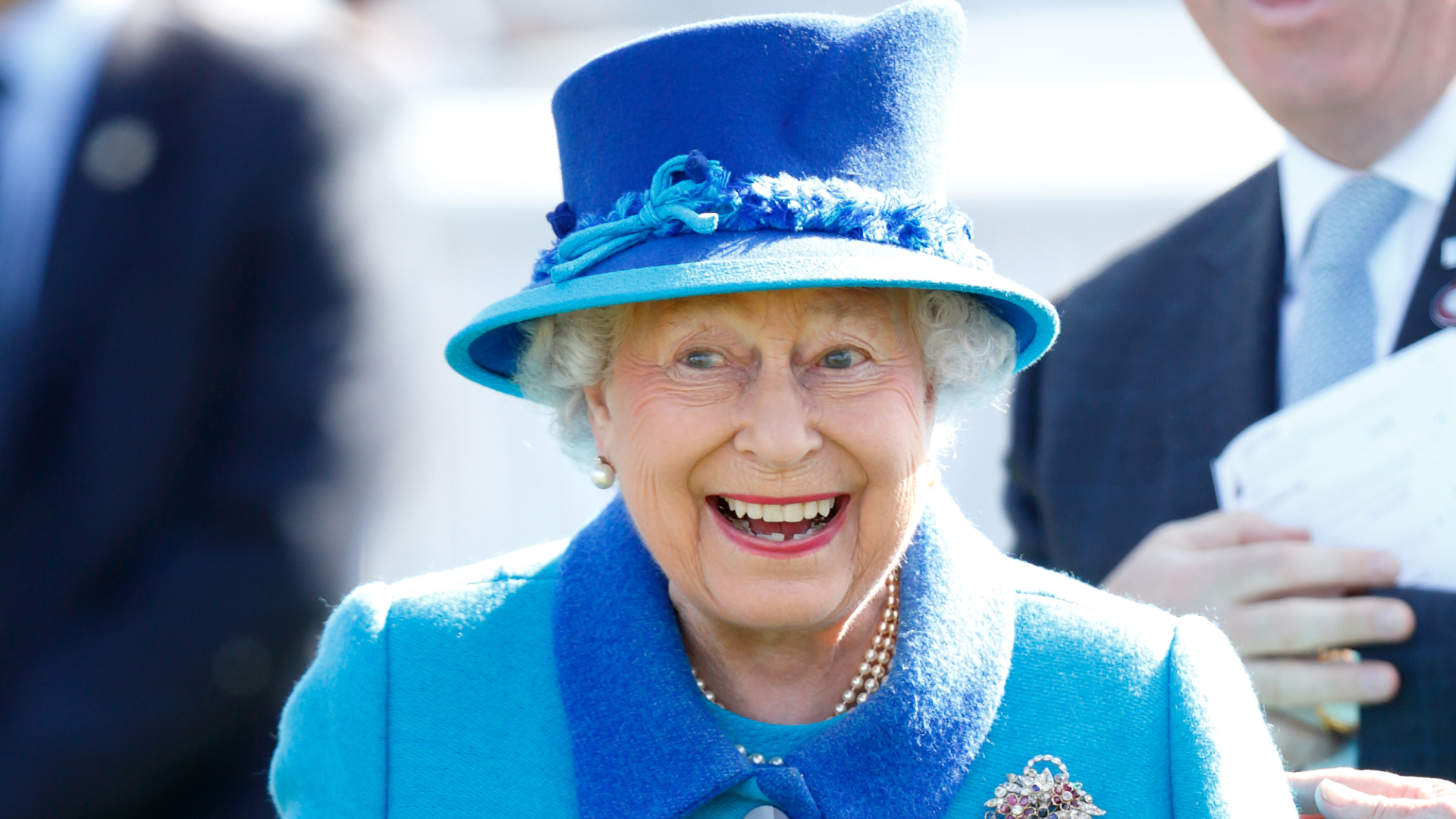 Queen Elizabeth wears a blue and turquoise coat with a matching hat