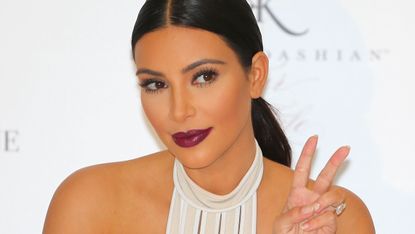 Kim Kardashian makes the peace sign with her fingers.