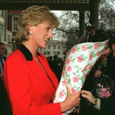 Princess Diana wearing a red suit holding flowers talking to fans