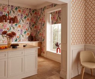 cream kitchen with pink, green and orange floral wallpaper, room to other side decorated with cream wall panelling and orange patterned wallpaper