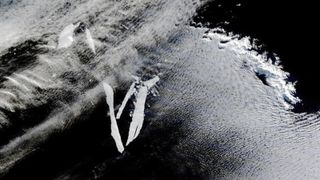 An aerial image of six tightly grouped iceberg fragments floating on the sea and partially obscured by cloud