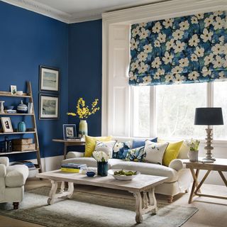 living room with blue wall white sofa with cushions wooden shelf and white window