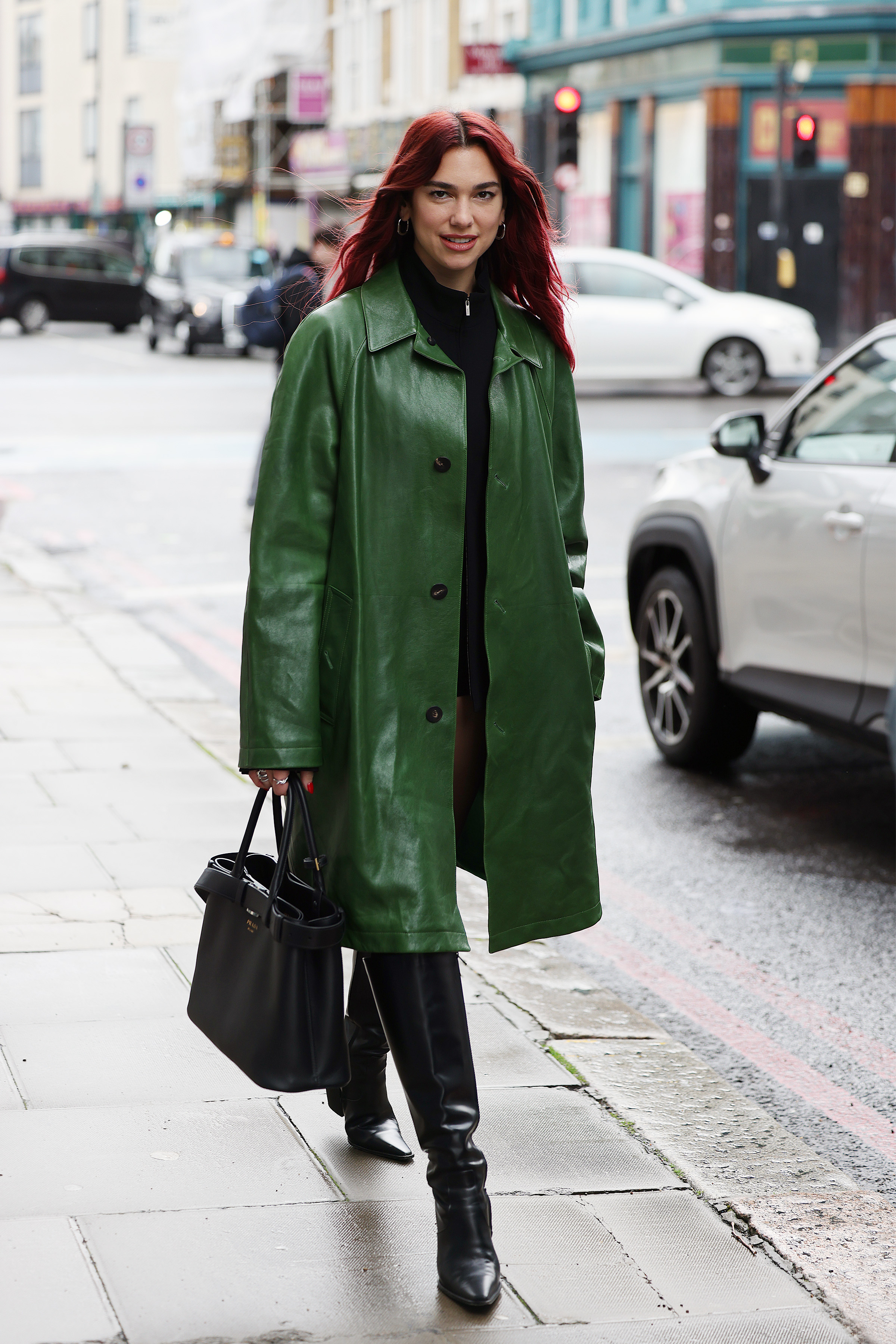 Dua Lipa wears a green leather trench coat with the Prada belt bag in hand.