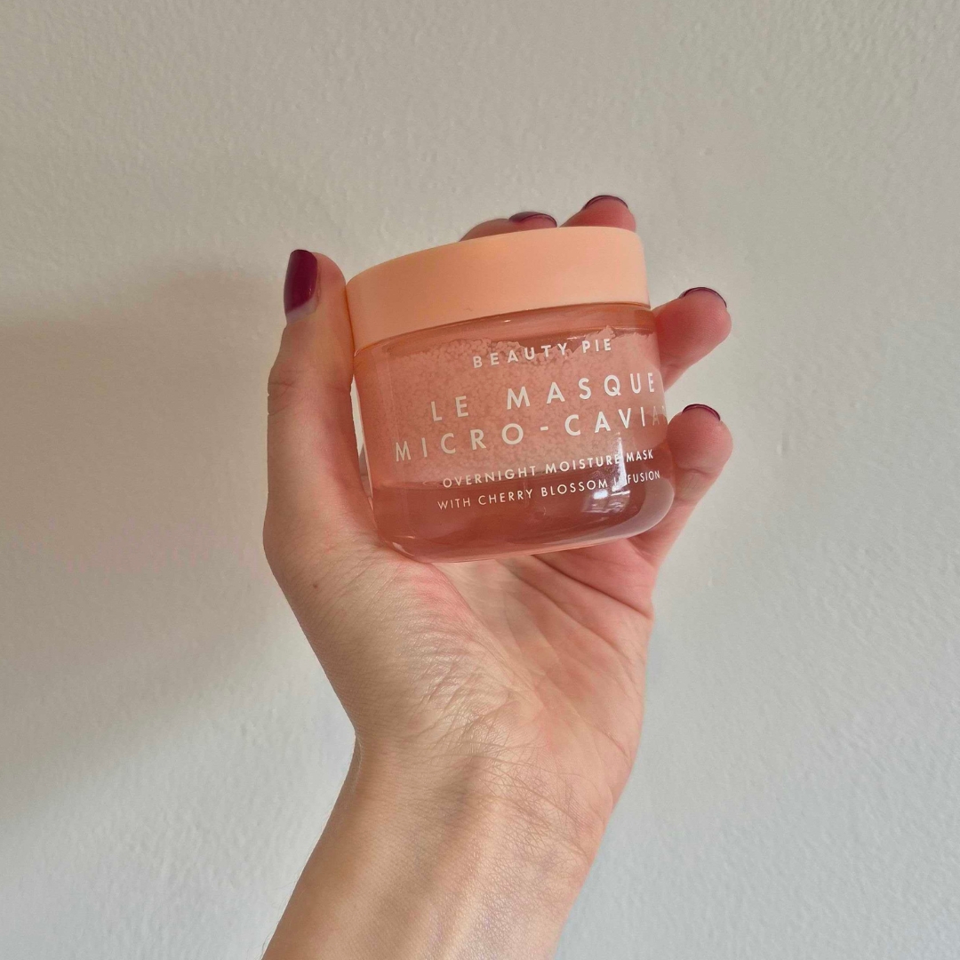 A close-up of Digital Beauty Writer, Naomi Jamieson holding up the Beauty Pie Le Masque Micro-Caviar Overnight Moisture Mask, in front of a cream wall