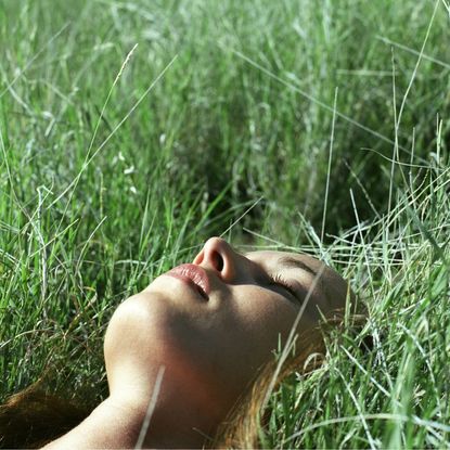 A woman lying in the grass trying the viral 5-4-3-2-1 grounding technique