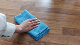Person using a blue microfiber cloth to clean laminate floors.