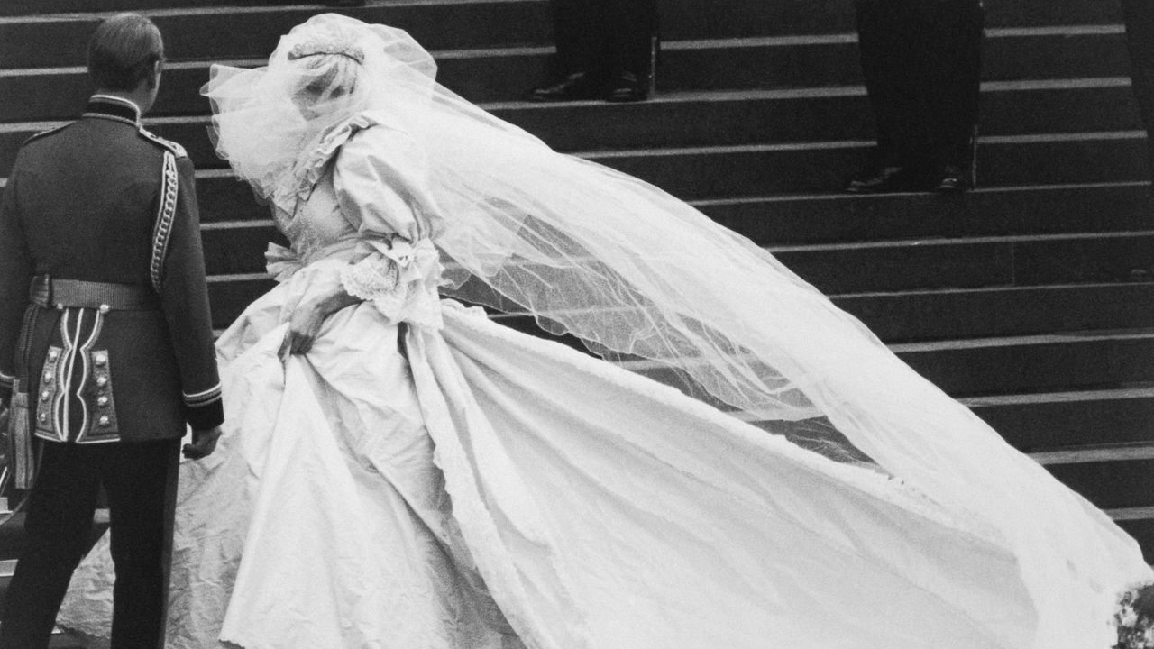 A black and white photo of Princess Diana walking up the stairs of St. Paul&#039;s Cathedral in her wedding dress in 1981