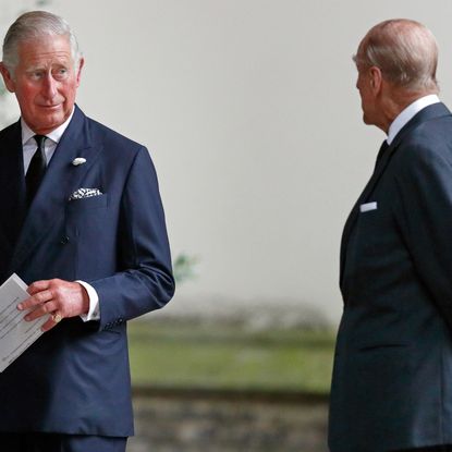 Prince Charles holding a paper and turning to look at Prince Philip
