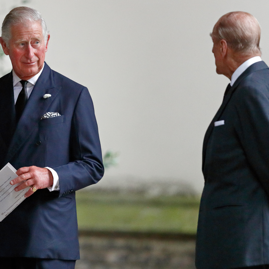 Prince Charles holding a paper and turning to look at Prince Philip