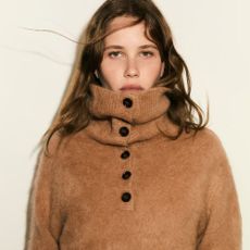 Woman wears beige funnel-neck jumper