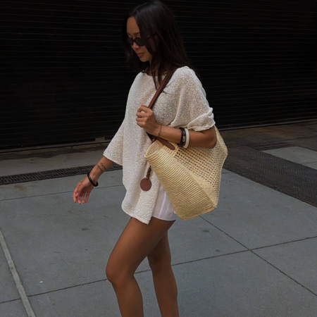 Woman wearing white shirt, raffia bag, and white shorts while wearing a ke summer 2026 shoe color trend, PVC shoes.