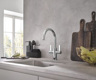 A sleek kitchen setup featuring a GROHE Eurosmart two-handled chrome kitchen mixer tap, paired with a stainless steel undermount sink. The minimalist concrete-effect backsplash complements the neutral countertop.