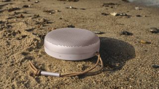 En ljusrosa Bang & Olufsen Beosound A1 ligger utomhus på en strand.