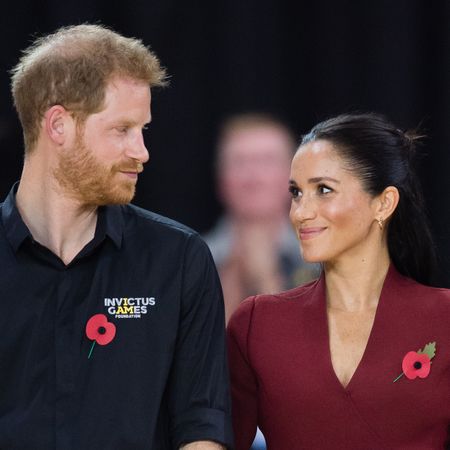 Prince Harry wears a black Invictus Games polo shirt and gazes adoringly at his wife, Meghan Markle, who is wearing a dark red V-neck top