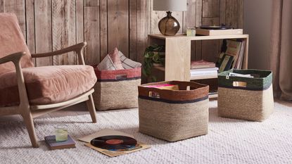 Hand-woven seagrass baskets on the floor of a living room, next to a wood and upholstered arm chair and a wooden storage shelf