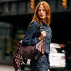 Fashion week attendee wearing denim set and dark red bag with scarf