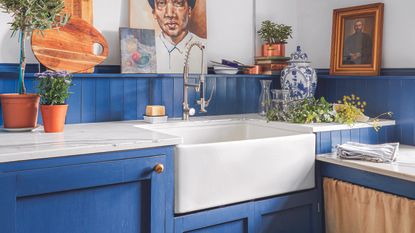 Utility room with navy wall panelling, oak counter and rattan baskets.