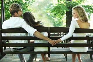 A man holds hands with another woman behind his partner's back.