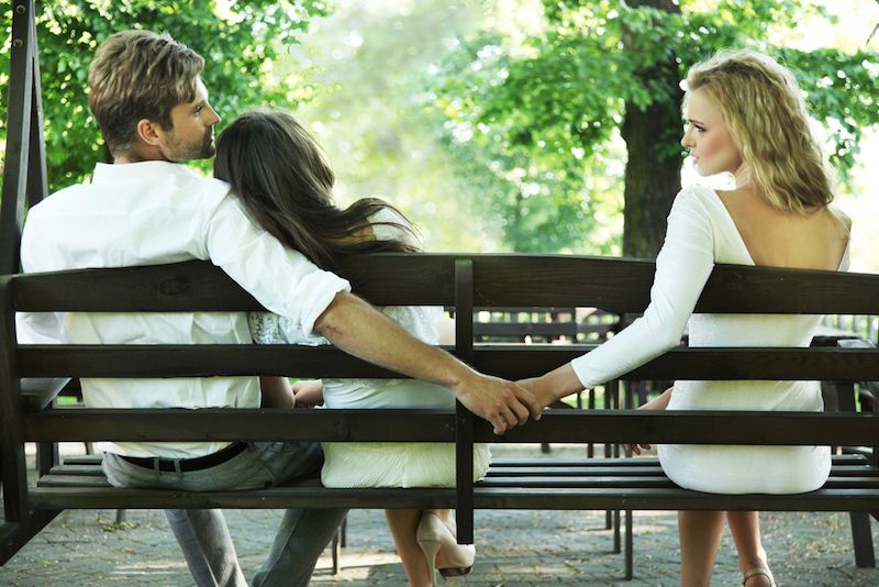 A man holds hands with another woman behind his partner&#039;s back.