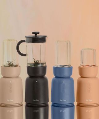 Four blenders lined up on counter with peach background