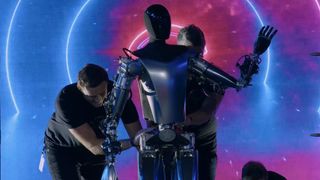 The Tesla Optimus humanoid robot being assisted by two human workers.